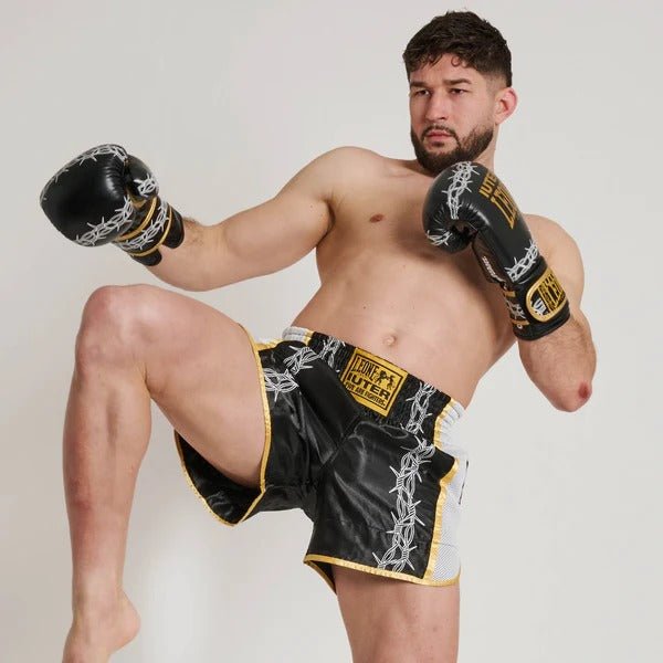 Atleta em pose de chute de Muay Thai mostrando flexibilidade de shorts de arame farpado