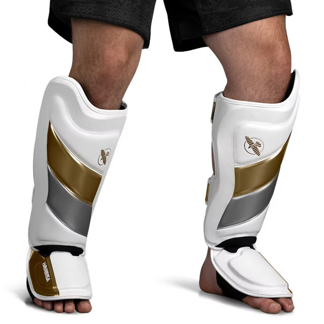 Vista frontale del parastinco Hayabusa T3 Striking bianco e oro, che mostra l'imbottitura pre-curvata