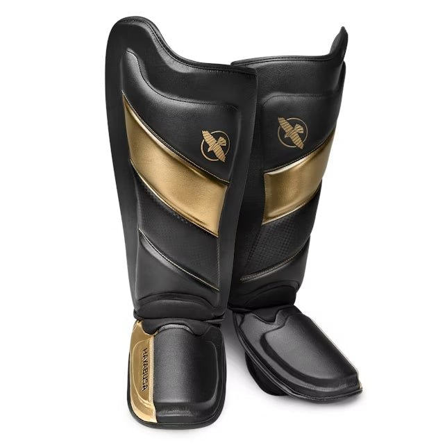 Pair of black and gold Hayabusa T3 Striking shin guards for kickboxing and MMA, front view