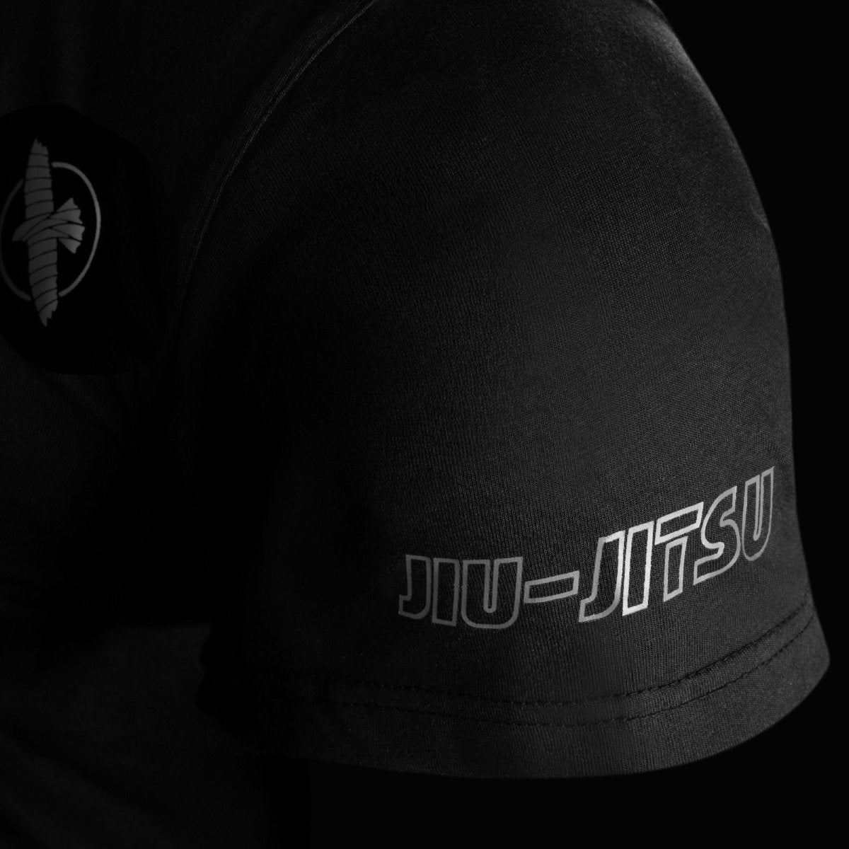Detail close-up lengan kaos Hayabusa UFC BJJ berwarna hitam, memperlihatkan jahitan yang diperkuat dan logo elang yang dibordir